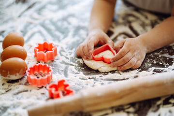 A little child  cutting out shapes heart dough. Easter baking preparation. Children's art project, a craft for children.