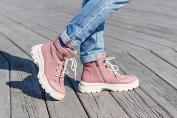 Women's feet in fashionable pink demi-season boots with white soles and laces on a wooden pier. Side view