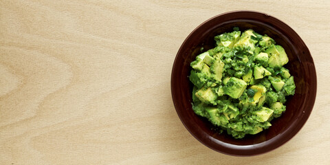 Bowl of freshly made chunky guacamole on wooden table with copy space for text, top view.
