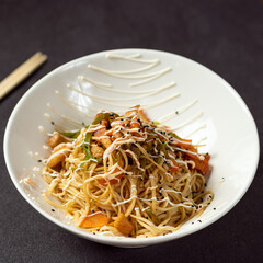 Chow mein noodles and vegetables dish with wooden chopsticks on the black background