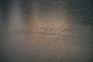Texture of golden calm water of lake in sunrise. Meditative ripples on water surface. Nature minimal background of gold lake in sunset. Natural backdrop of clear water. Full frame of lake fragment.