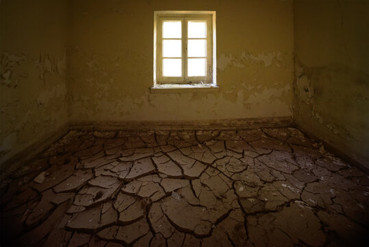 Abandoned house interior. Room with cracked clay on the floor and peeling yellow paint on walls