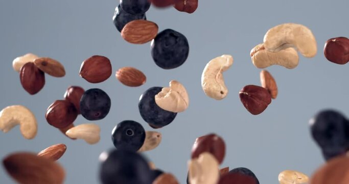 SUPER SLOW MOTION mixed pile of cashew, hazelnut and almond nuts flying along with blueberries against light blue background. Shot with high speed video camera, 720 FPS