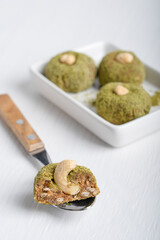 Organic sweet vegetarian truffles or homemade nut vegan energy balls made of cashew, hazelnut and walnut in green powder served on plate with spoon on white wooden table ready for eating. Vertical