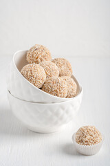 Organic sweet truffles dessert or homemade nut vegan energy balls made of sesame, hazelnut and dates fruit served in two bowls standing one inside the other on white wooden table. Vertical image