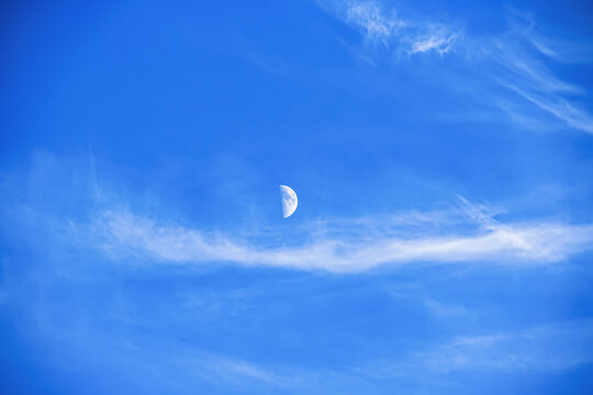 Close-up of the July sky. On a warm summer day, soft clouds and the moon met in a bright blue sky. Natural beauty. Russia