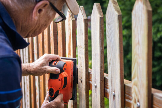 Sanding wooden plank. Senior man grinding picket fence with sander