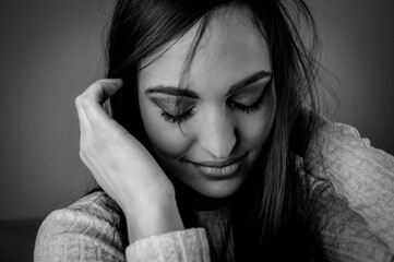 Black and white portrait of a beautiful young woman with long dark hair who shyly looks down while...