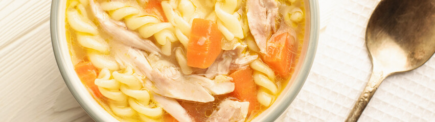 Close up of a bowl of chicken noodle soup with spoon banner