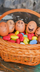 Stack of eggs with hand drawn faces on straw basket with colorful candy, easter preparation, holiday mood concepts