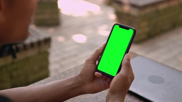 close up man holding smartphone with green screen video call outdoors