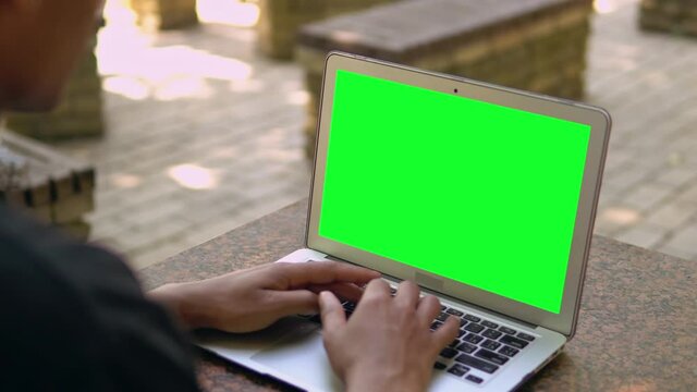 unrecognizable man typing on laptop with green screen mixed race guy chatting online or shopping or working outdoors