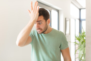 handsome man raising palm to forehead thinking oops, after making a stupid mistake or remembering,...