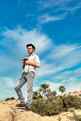 A young traveler man standing on a rock while holding a photo camera