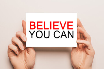 Female hands hold card paper with text Believe you can on a yellow background. Business and finance concept