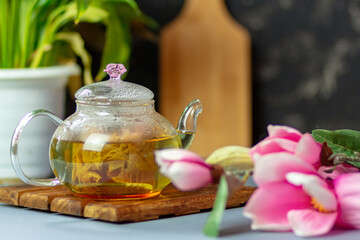 green tea with rose petals in a transparent teapot on a wooden table on a black background. The background is blurred. Tea drinking.