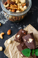 Homemade chocolate fudge garnished with mint leaves and served with tea on a black background. Nuts in the background blurred background. Copy space.