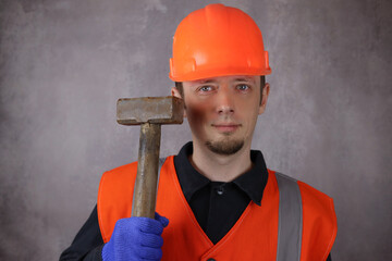 Young male worker with old hammer, sledgehammer on gray background
