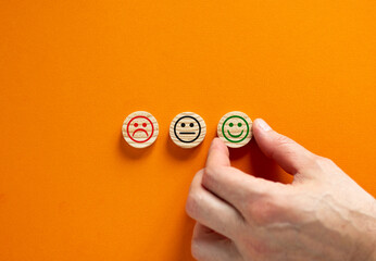 Various emoticons made of wooden circles drawn lines of a mouth. Over orange background in a conceptual image of quality and feedback. Customer hand. Business and feedback concept.