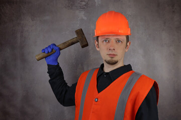 Young male worker with old hammer, sledgehammer on gray background