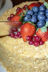 Kitchen knife cutting cake decorated with berries.