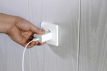Hand turns on, turns off charger in electrical outlet on wall