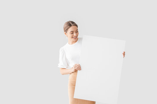 Beautiful young woman with blank poster on light background
