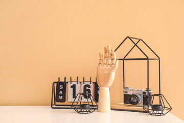 Wooden hand with calendar, photo camera and candles on table near color wall in room