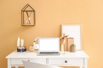Wooden hand with laptop and photo camera on table near color wall in room