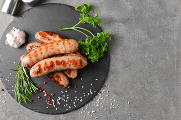 Slate plate with delicious grilled sausages on grey background