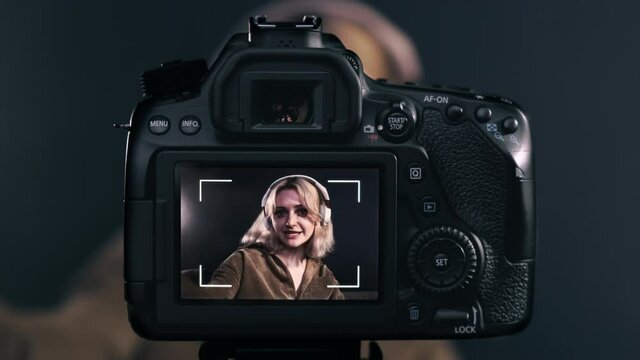 Young content creator blonde talking girl filming herself using a camera on a tripod while recording a vlog. Working from home