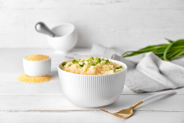 Bowl with tasty couscous and green onion on light wooden background