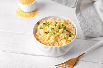 Bowl with tasty couscous and green onion on light wooden background