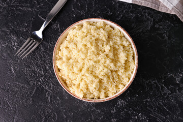 Bowl with tasty couscous on dark background