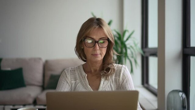 Front view of businesswoman working with laptop and sitting at table in modern home office.