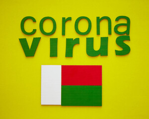 Flag of Madagascar And Word CORONAVIRUS made of green cardboard letters, isolated on yellow background. World Health Organization WHO introduced new official name for Coronavirus disease named COVID