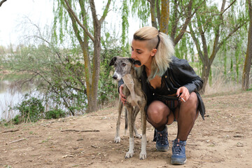 Young punk woman smoking and biting her greyhound dog ear in a park. Rock and roll lifestyle.