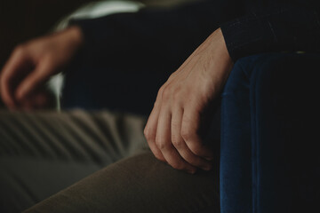 The man sits next to the wall looking forward, the room is dim