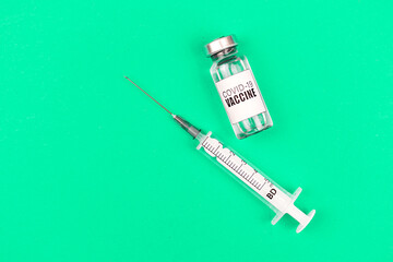 Vial with coronavirus vaccine and medical syringe on a green background, top view and copy space