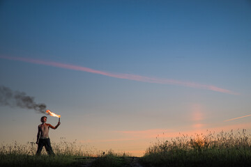 Man stands with signal torches against dark sunset sky
