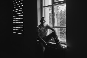 A man in a T-shirt sits by the window