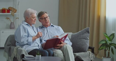 Two old people elderly couple missed husband and wife sitting on sofa in cozy living room remember pleasant moments from past looking at pictures of their beloved children,turn pages of photo album - Powered by Adobe