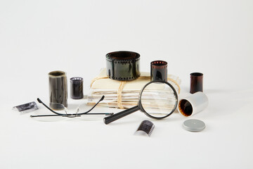 A stack of old photographs, negatives, glasses and a magnifier on a white background.
