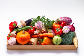 Assorted organic vegetables in a wooden box on a light background.