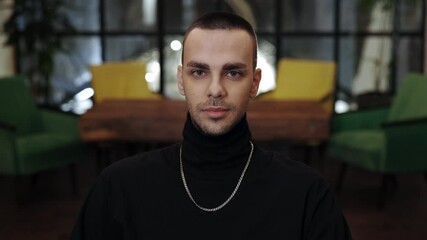 Portrait of young stylish caucasian guy raising head and looking to camera. Portrait of handsome man with bristles and chainlet posing. Blurred background.