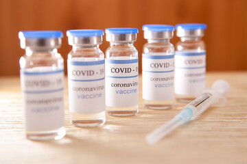 Vaccine ampoules and syringe, coronavirus medical concept on brown background