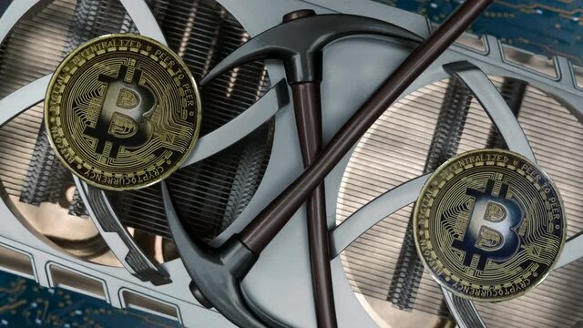Cooling fans are spinning on the video card, Bitcoin coins shine in the light and two pickaxes as a symbol of cryptocurrency mining using computer video cards. Macro. Closeup
