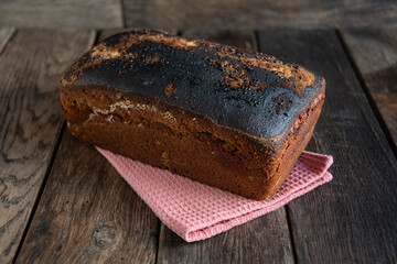A loaf of homemade bread lies on a kitchen napkin, on a wooden table.