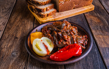 Pickled eggplants, tomato, cucumber, and pepper in earthenware on a wooden table. Homemade pickles. Homebaked bread.