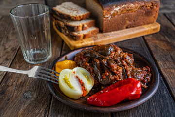 Pickled eggplants, tomato, cucumber, and pepper in earthenware on a wooden table. Homemade pickles. Homebaked bread.